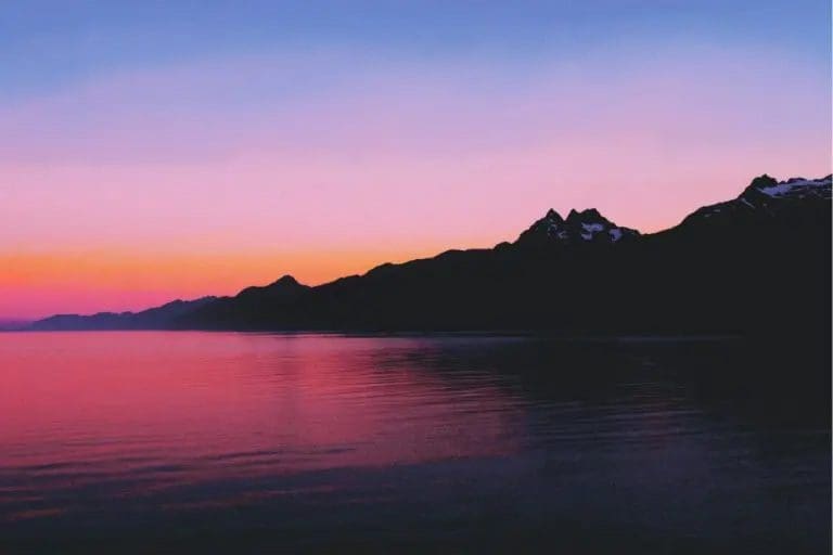 freezydreamin-LXw-Dg0H4is-unsplash-768x512 - Suzanne Kane A serene sunset casts vibrant colors over mountains, reflecting beautifully on the calm water below.
